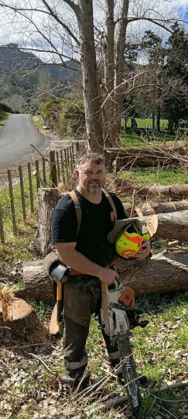 Trees2Timber owner-operator Philip Rae with his chainsaw beside a stack of fresh logs